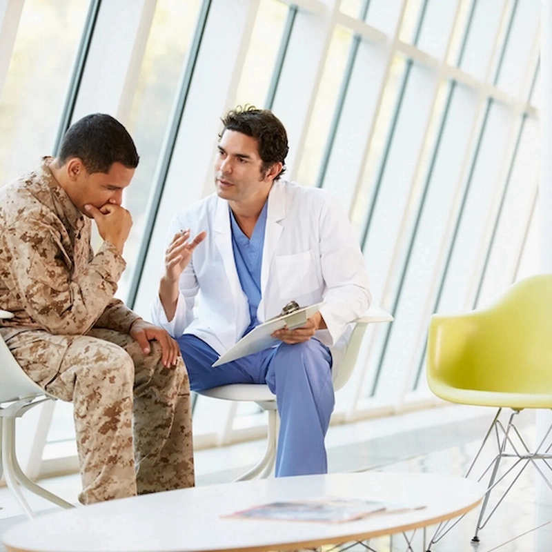 A military veteran in uniform discussing treatment options with a compassionate doctor, highlighting the specialized support available for combat-related PTSD at Serenity Grove.