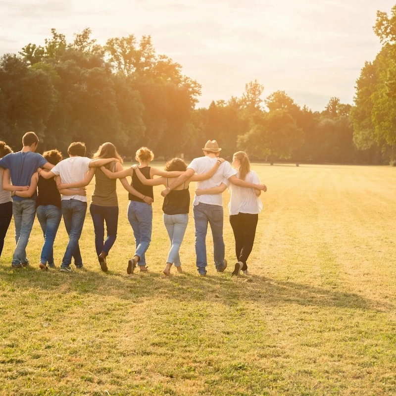 A group of people stands with linked arms in a sunny field to symbolize the strength of mental health support and community.