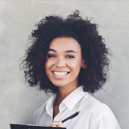 A portrait of a smiling woman with curly dark hair holding a clipboard and pen at a mental health facility