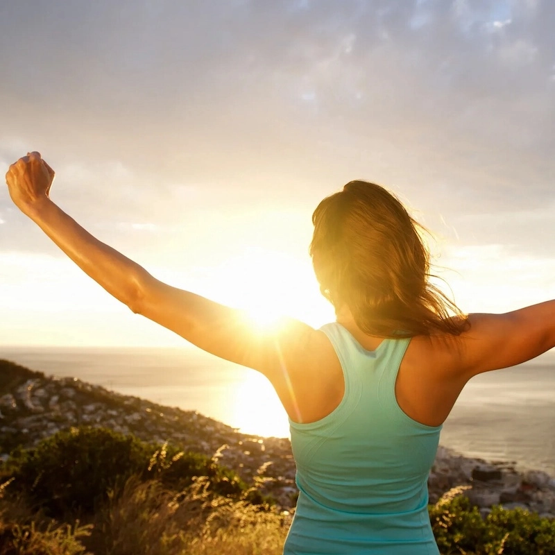A woman raises her arms toward a golden sunrise, symbolizing the hope, freedom, and stability found in effective bipolar disorder treatment at Serenity Grove.