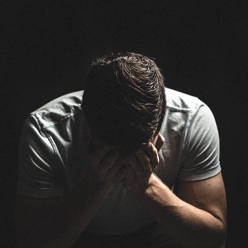 A man sitting in the dark with his head buried in his hands, symbolizing the intense isolation, despair, and emotional burden often experienced by those living with PTSD.