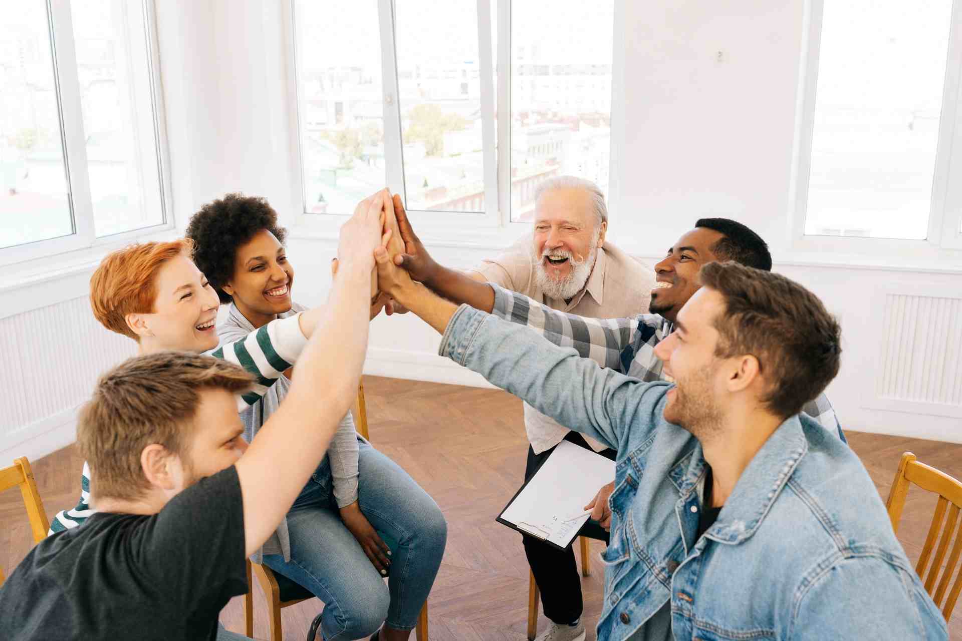 Diverse group in mental health therapy session celebrating progress with a group high five