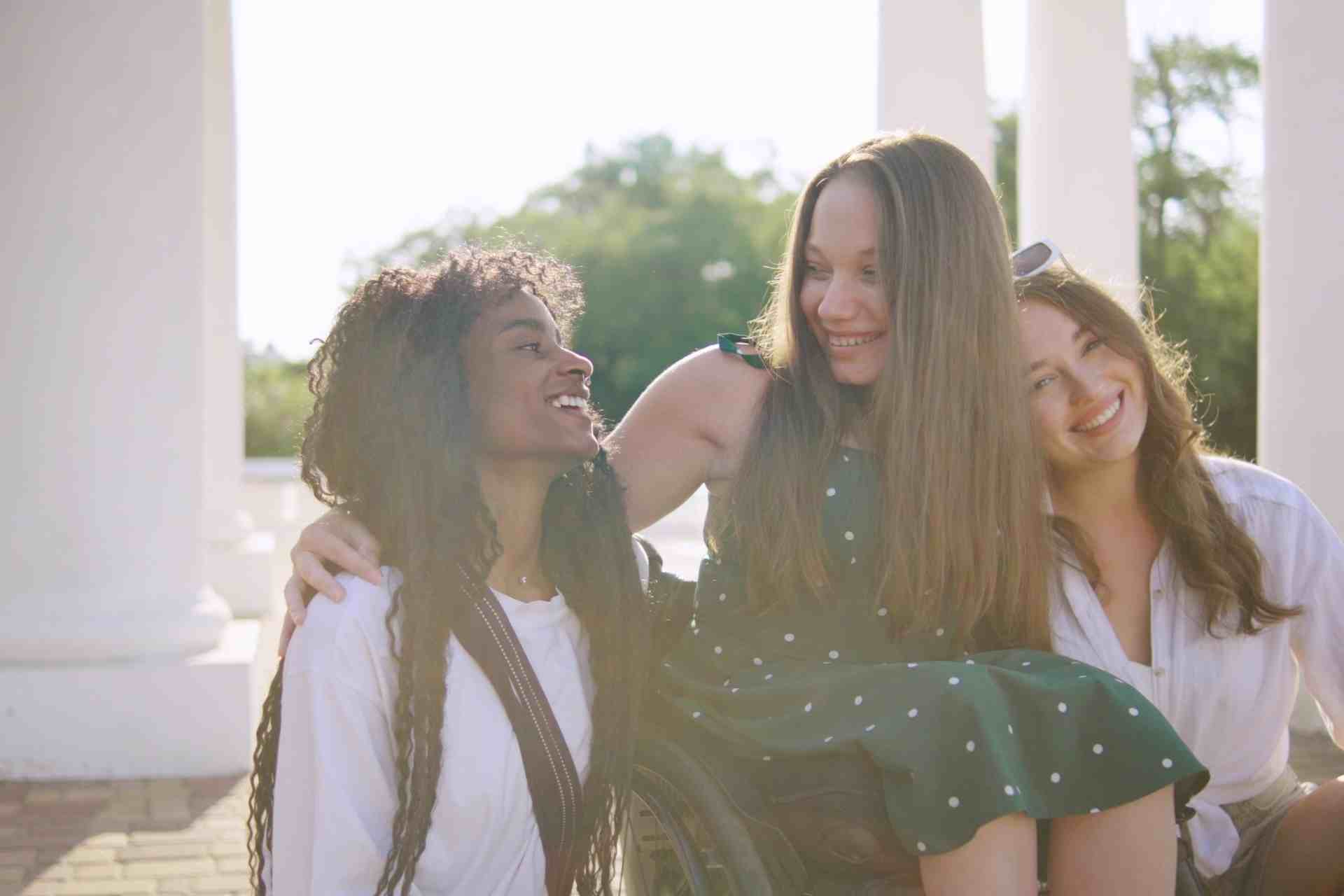 Three young women smiling together outdoors, representing friendship, emotional support, and mental health recovery.