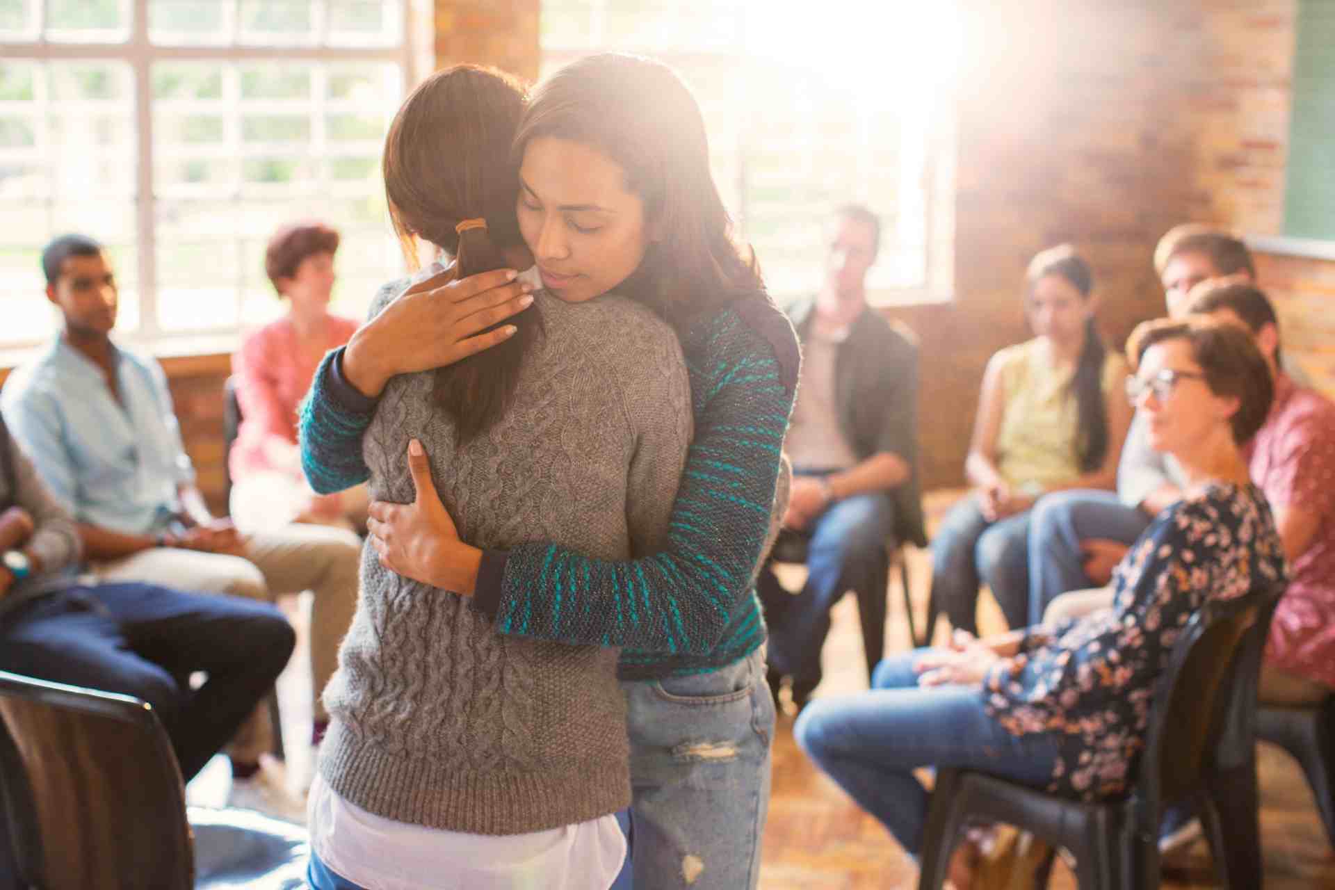Two women hugging during group therapy mental health support session