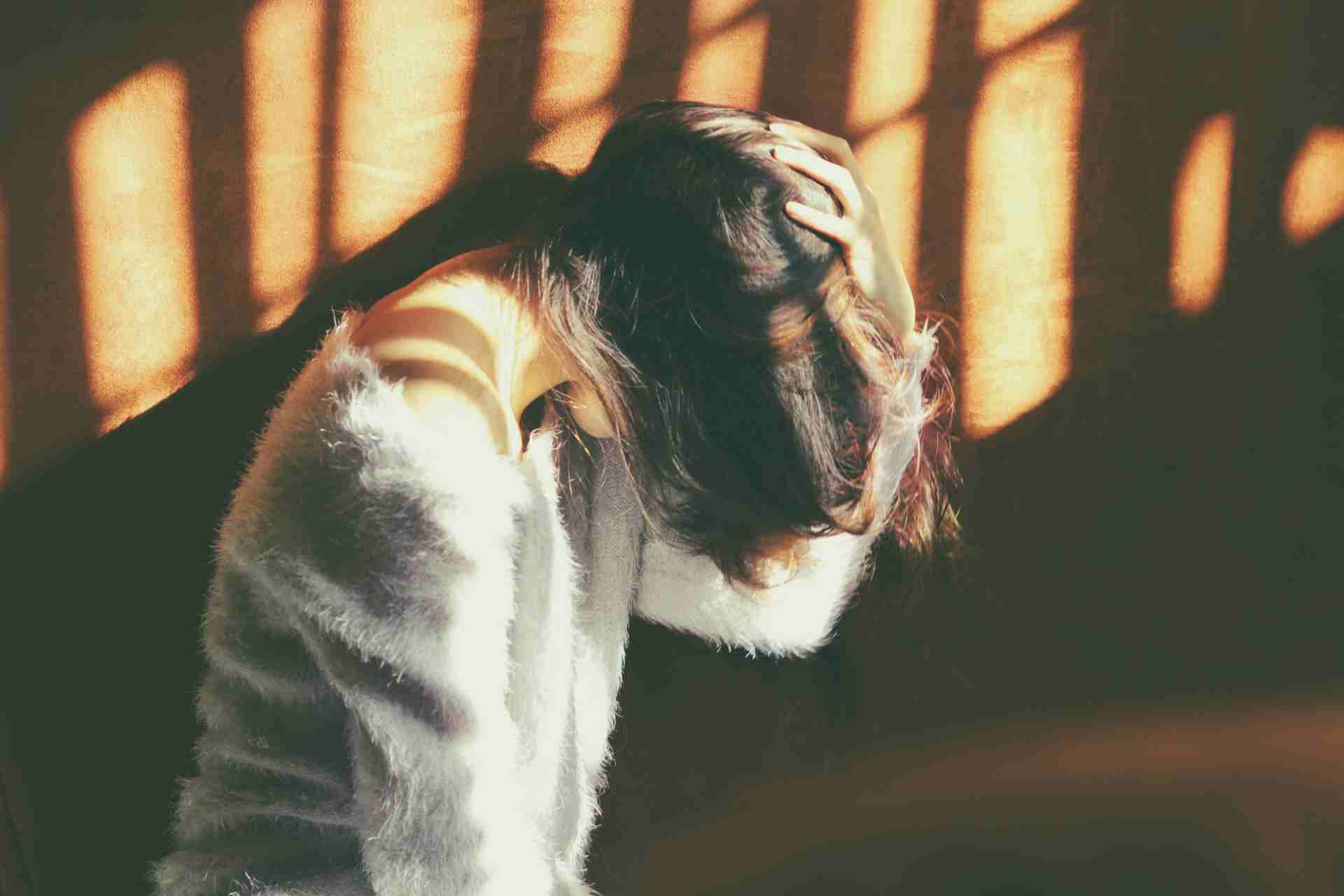 Woman sitting alone with her head down and hands in her hair, showing signs of emotional stress and anxiety