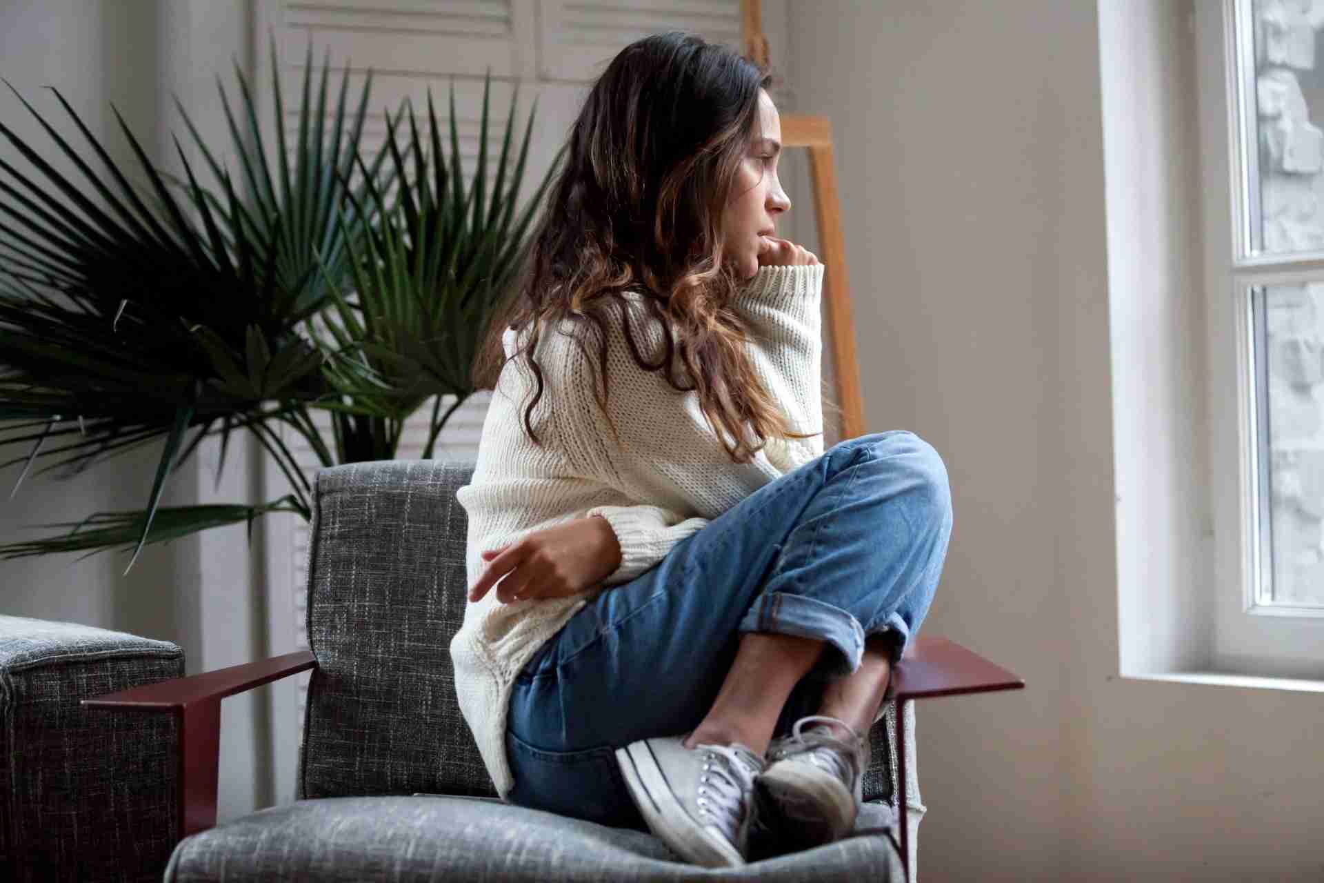 Young woman sitting alone and looking out a window while experiencing anxiety, stress, or depression