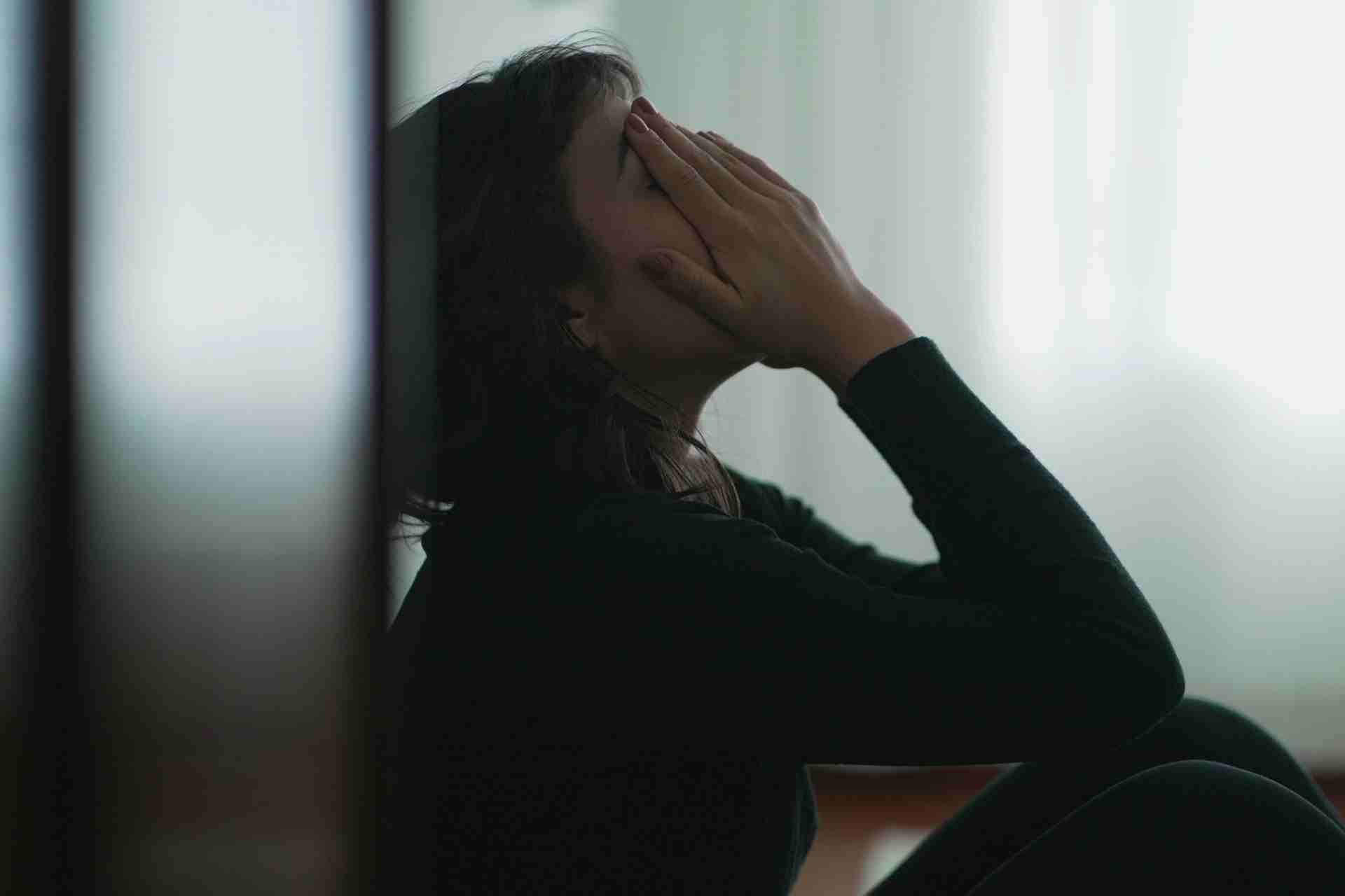 Woman sitting alone with her face in her hands showing emotional exhaustion and signs of functional depression.