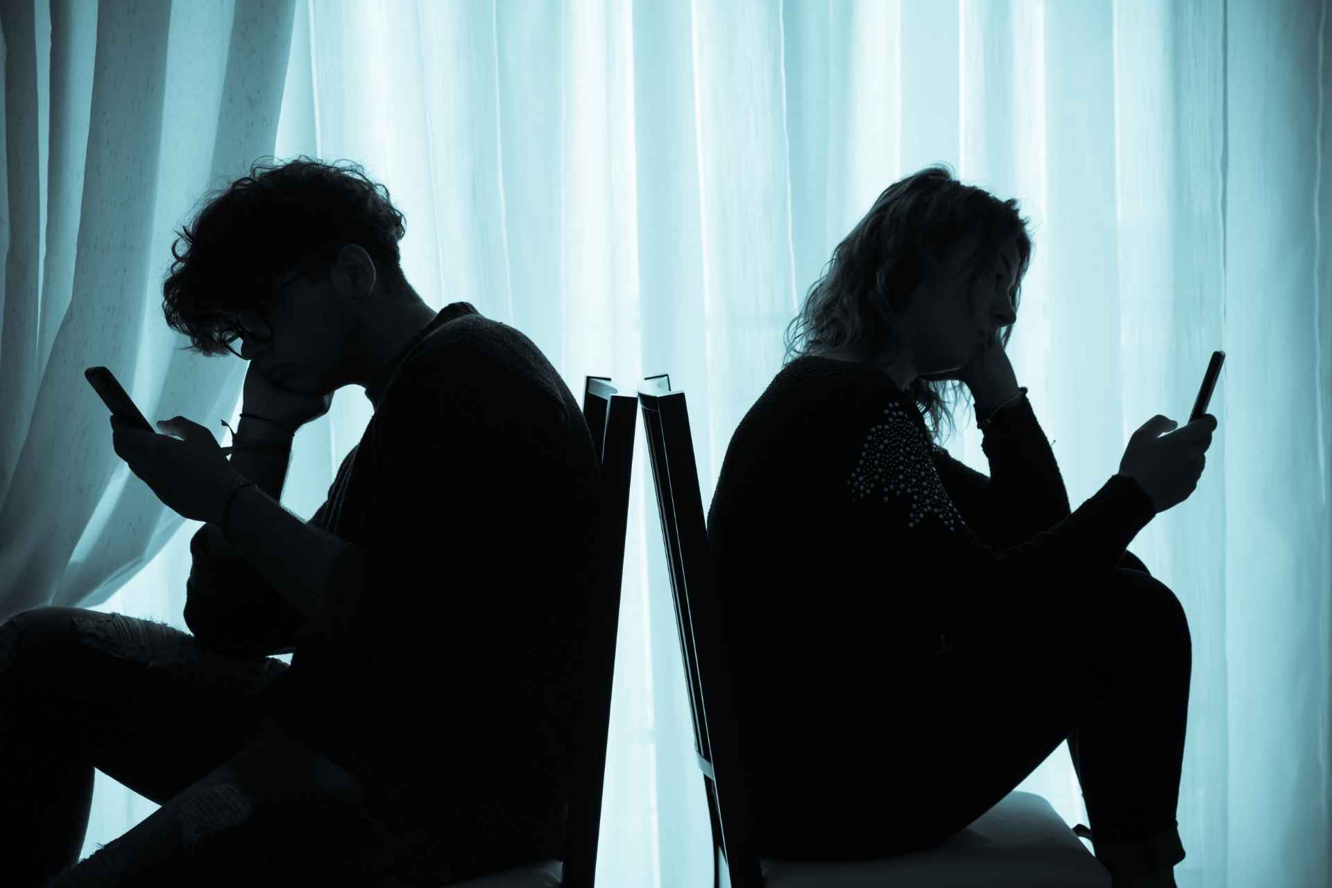 Couple sitting back-to-back absorbed in phones, illustrating loneliness versus social isolation