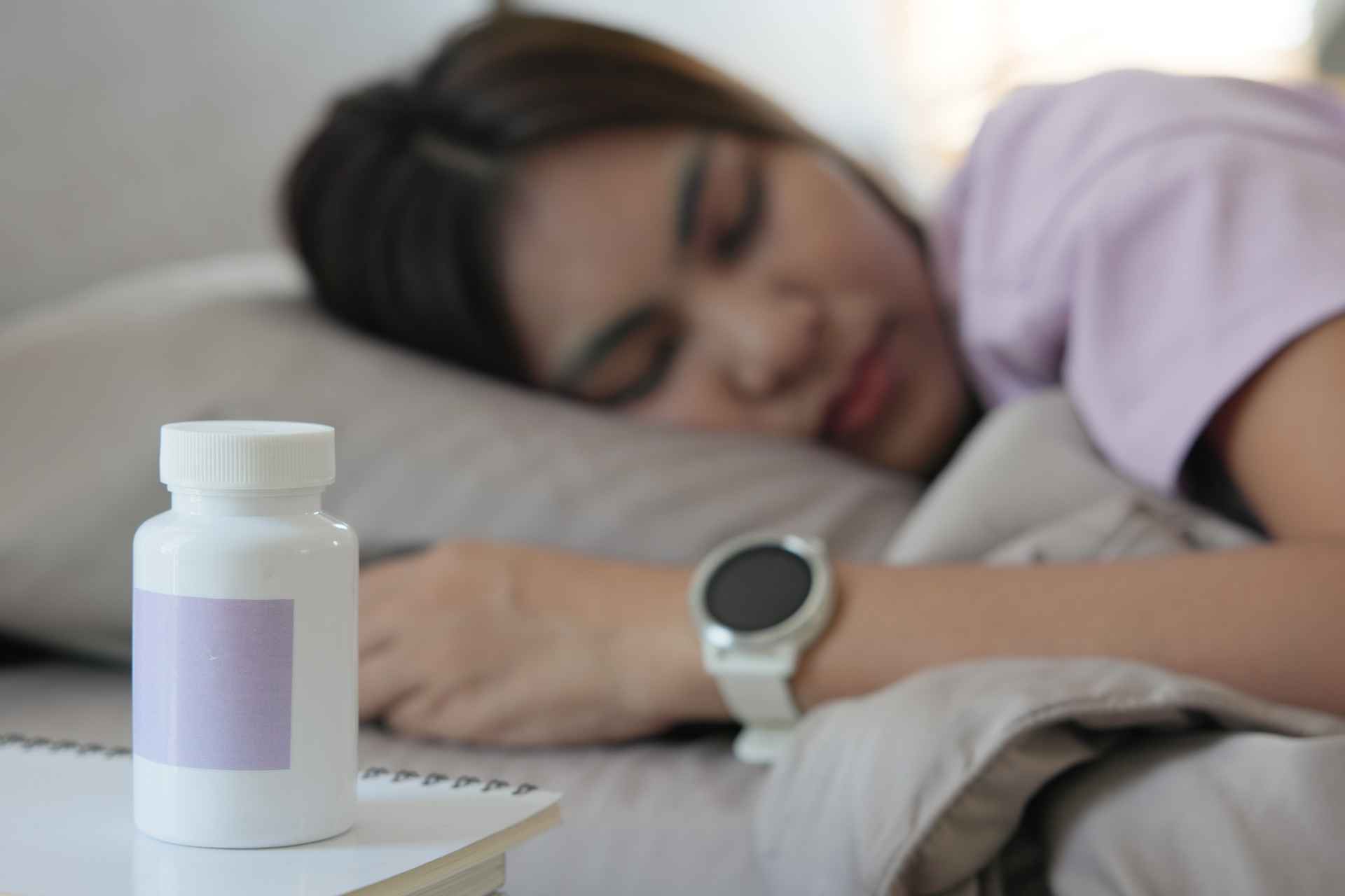 Person sleeping with a medication bottle on a bedside table