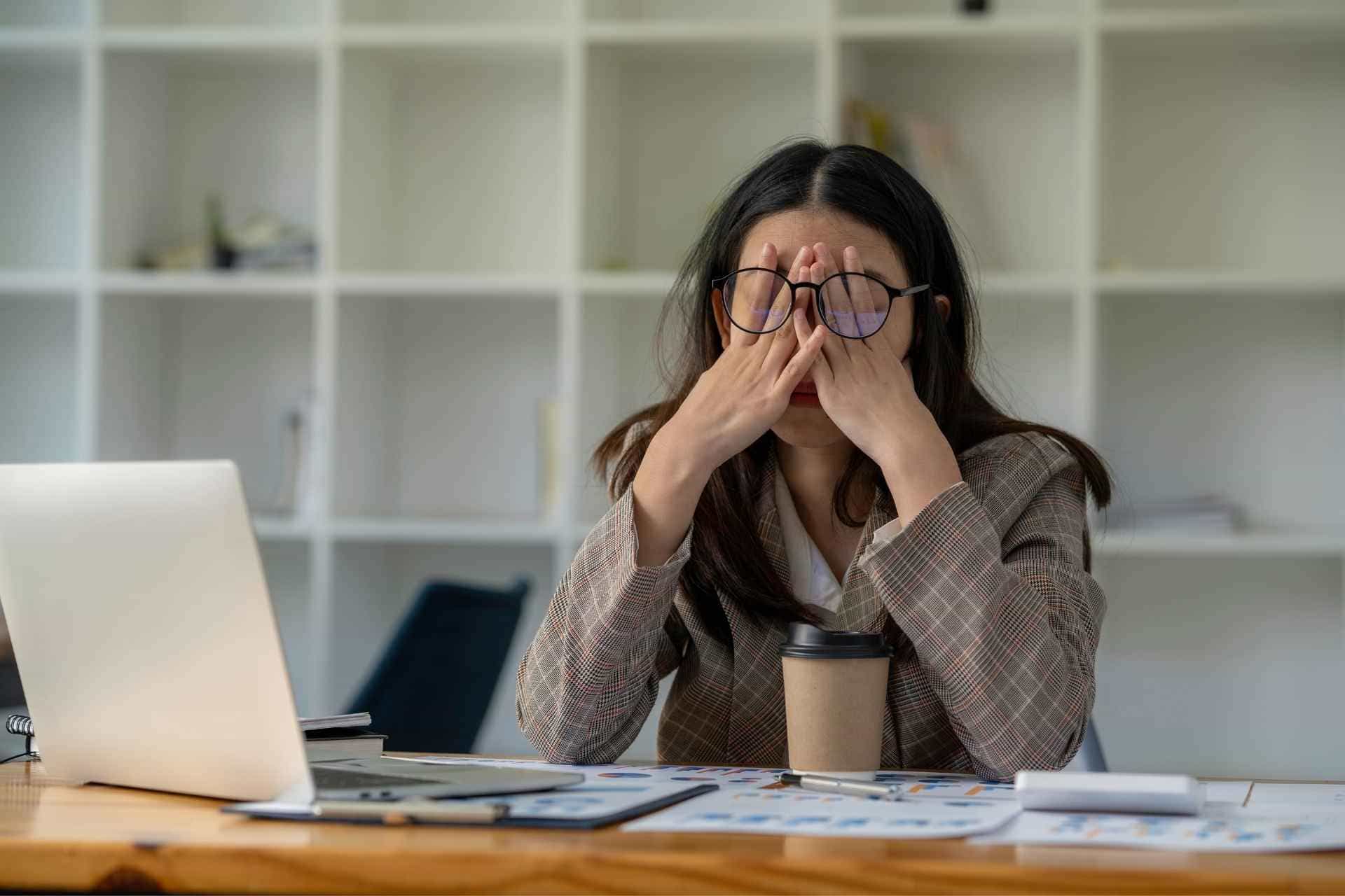 Woman with face in hands at work desk experiencing work stress