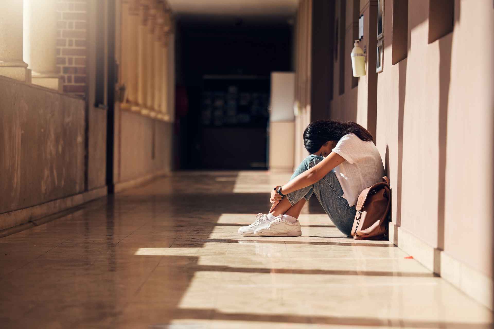Teen girl sitting alone in a school hallway, showing signs of social isolation